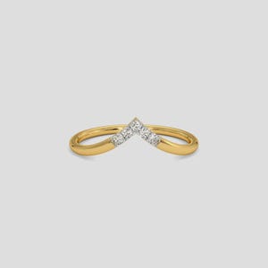 May include: A gold-colored ring with a V-shaped design. The ring features small, clear gemstones set in the center of the V. The band is smooth and rounded, creating a delicate and elegant appearance.