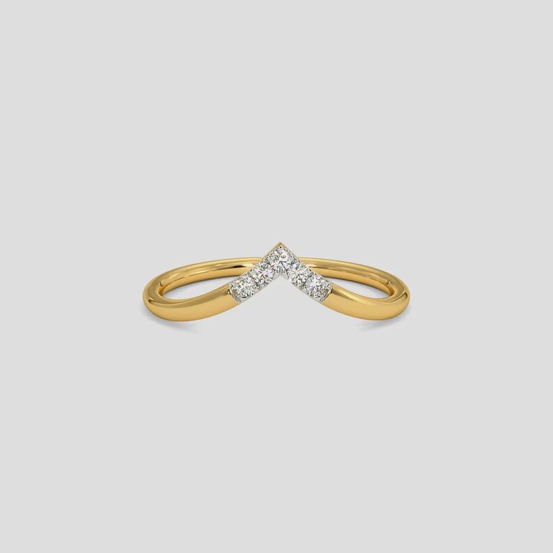 May include: A gold-colored ring with a V-shaped design. The ring features small, clear gemstones set in the center of the V. The band is smooth and rounded, creating a delicate and elegant appearance.