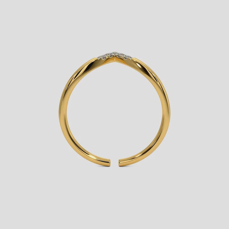 May include: A gold-colored ring with a V-shaped design at the top, adorned with small, sparkling stones. The ring has a smooth, polished finish and an open design. The ring is set against a light gray background.