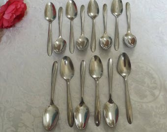 May include: A set of 12 silver teaspoons with a polished finish. The spoons are arranged in two rows of six, with the handles pointing towards the center.
