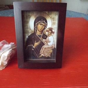 May include: A framed religious icon depicting the Virgin Mary holding a baby Jesus. The icon is painted in a traditional style with gold accents and a dark background.