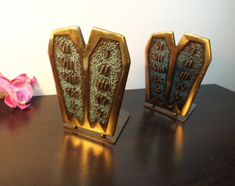 May include: A pair of gold-toned bookends shaped like the Ten Commandments tablets. The tablets are decorated with Hebrew text and have a green patina.