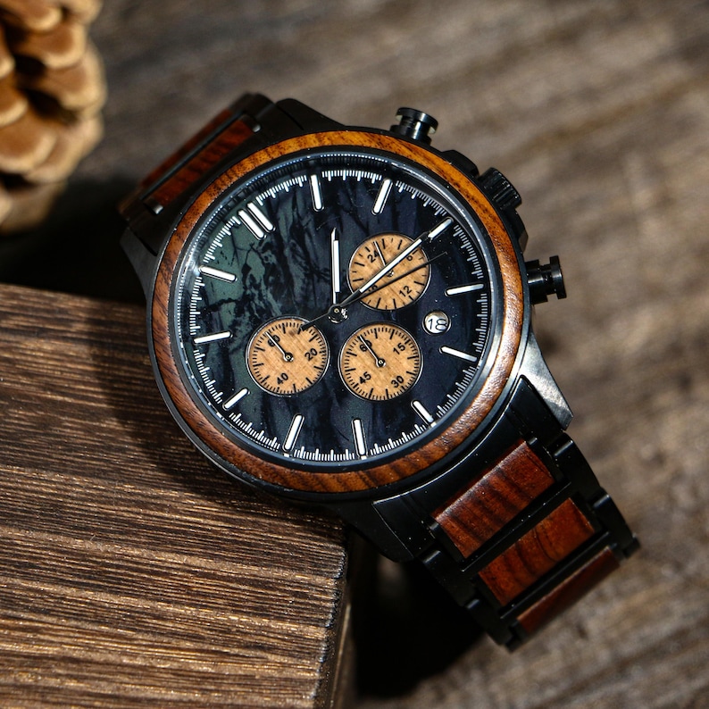 May include: A black and wood-toned chronograph watch with a dark face and three sub-dials. The watch features a wooden bezel and band, with a black metal case. The watch face has white markers and hands.