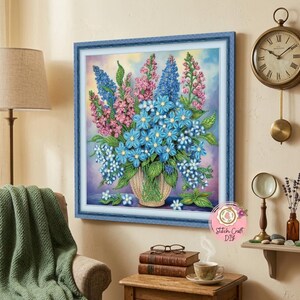 Peut inclure: Une broderie florale encadrée représentant un bouquet de fleurs bleues, roses et blanches dans un vase tissé. L'œuvre est placée sur un fond coloré, avec un cadre bleu. Un objet décoratif.