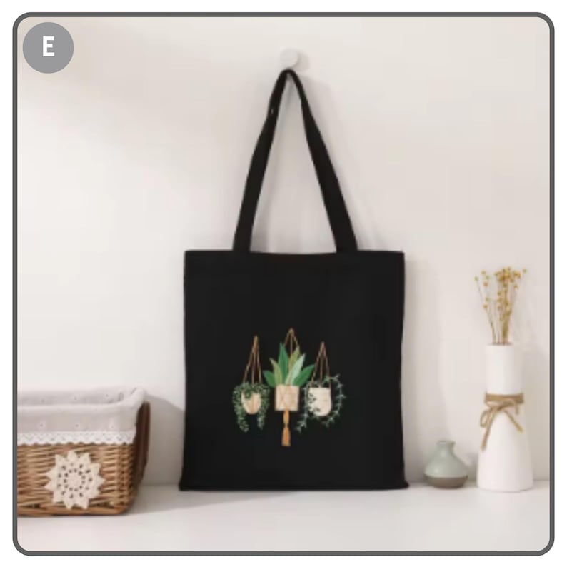 Puede incluir: Bolso tote negro con un dise&ntilde;o bot&aacute;nico de plantas colgantes. El bolso tiene forma rectangular y asas largas. Las plantas est&aacute;n representadas en tonos verdes y marrones.