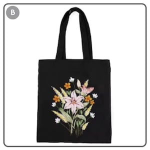 Puede incluir: Bolso tote negro con dise&ntilde;o floral bordado. El dise&ntilde;o presenta un gran lirio rosa, flores naranjas y blancas y hojas verdes. El bolso tiene dos asas negras.