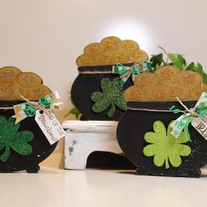 May include: A white ceramic mug with a black handle and the text "But First, Coffee" in a bold, black font. The mug is set against a blurred background, suggesting a cozy setting.