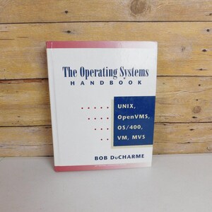 May include: A white hardcover book titled The Operating Systems Handbook by Bob DuCharme. The cover features dark blue text and a dark blue rectangular graphic containing the words UNIX, OpenVMS, OS/400, VM, MVS with red dots.
