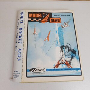 May include: A vintage "Model Rocket News" magazine. The cover features illustrations of rockets launching, a pilot in a helmet, and a small airplane. The magazine's spine reads "Model Rocket News Library Collection". The Estes Industries logo is visible.