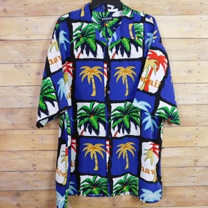 May include: Blue button-down shirt with a tropical print featuring palm trees in green, yellow, and red. The shirt has short sleeves and a collared neckline. The word "Koman" is visible on the collar.