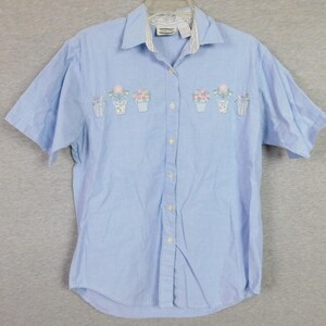 May include: A light blue short-sleeved button-down shirt with embroidered floral designs. The shirt has a white collar and a white button placket.