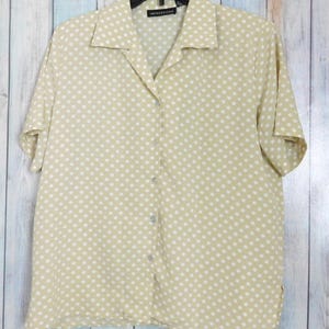 May include: A short-sleeved button-down shirt in a light beige color, covered in a pattern of white polka dots. The shirt has a classic collar and is labeled "Impressions" at the neckline.