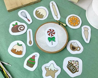 May include: A collection of embroidered patches with a baking theme, including a rolling pin, whisk, and a candy cane. A wooden embroidery hoop holds a candy cane patch. The patches are arranged on a green surface.