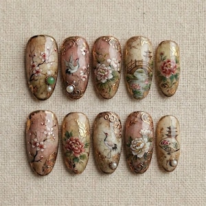May include: A collection of ten almond-shaped false nails, each hand-painted with detailed Asian-inspired designs. The nails showcase cherry blossoms, cranes, and pagodas, enhanced with gold leaf. The colour scheme includes soft pinks, creams, and browns, creating an elegant aesthetic.