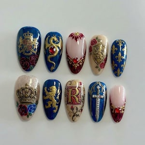 Puede incluir: Diez uñas postizas en forma de almendra, decoradas con diseños heráldicos, dragones, flores de lis y coronas, en tonos dorados, rojos y azules. Algunas uñas presentan rosas y joyas. Fondo blanco.