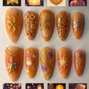 May include: A set of eleven nail designs in shades of orange and gold, featuring intricate details. Designs include floral patterns, sun motifs, and lantern illustrations. The nails are arranged on a white surface, with additional images of lanterns and a sun crest.