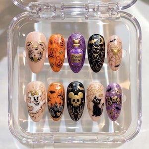 May include: A set of ten almond-shaped press-on nails in a clear plastic case, featuring Halloween designs including pumpkins, black cats, spider webs, ghosts, skulls, and a purple bottle with the text SPOOKY BREW and BOO with mouse ears.