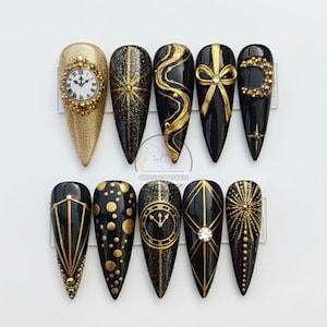 May include: A collection of ten long, almond-shaped artificial nails. The nails display black and gold designs, including a clock face, starbursts, swirls, bows, and geometric patterns. Some nails have a glittery finish, while others are matte. The overall theme is elegant and festive.