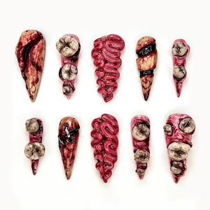 May include: A collection of ten grotesque, handmade nail art designs. Each nail features a unique, disturbing design, including exposed teeth, brain-like textures, and blood-red accents. The nails are arranged on a white background.