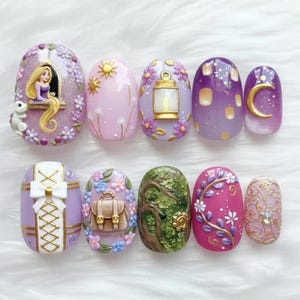 May include: A set of ten intricately designed artificial nails. Each nail features a unique design, including a princess, sun, lantern, and floral accents. Colors include purple, pink, gold, and green. The nails are arranged on a white surface.