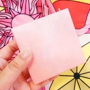 May include: A square, light pink box with a subtle, embossed feather or leaf pattern across its surface. The box has a smooth, matte finish and clean, sharp edges, presenting a simple, uniform appearance without any additional text or markings.