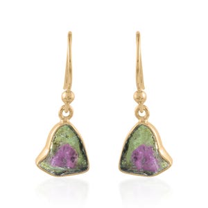May include: A pair of gold-colored drop earrings. Each earring features a green and pink gemstone in a bell-like shape. The gemstones have a natural, organic appearance, with a mix of green and pink hues.