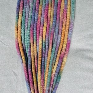 May include: A bundle of colorful dreadlocks in shades of pink, purple, blue, green, and yellow. The dreadlocks are arranged vertically against a white background, showcasing a gradient of colors.