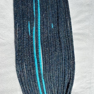 Könnte beinhalten: Eine Ansammlung dunkelblauer Dreadlocks mit einem leuchtenden türkisfarbenen Streifen in der Mitte. Die Dreadlocks liegen auf einer weißen Oberfläche, wodurch ihre Textur und Farbvariationen hervorgehoben werden.