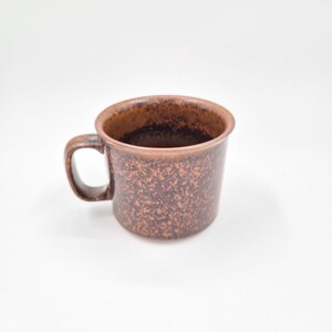 Peut inclure: Une tasse en céramique marron avec un motif moucheté. La tasse a un corps arrondi, une anse et un bord légèrement évasé. L'intérieur de la tasse est d'une teinte plus foncée de marron. Idéale pour le café ou le thé.