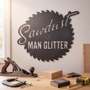 May include: A black circular metal wall sign shaped like a saw blade with the text Sawdust is MAN GLITTER cut out from the center. The sign is displayed above a wooden workbench featuring a hand plane, a metal C-clamp, a wooden block, and a tape measure.