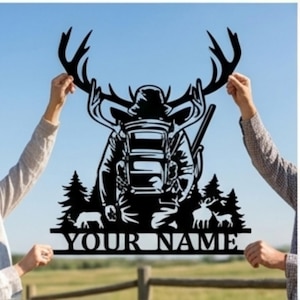 May include: A black metal wall sign featuring a silhouette of a hunter with a backpack and rifle, framed by large deer antlers. The design includes pine trees, smaller deer figures, and a horizontal bar at the bottom with the text YOUR NAME.