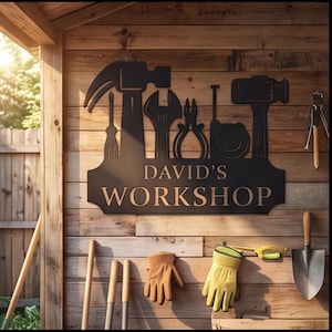 May include: A black metal wall sign featuring silhouettes of a hammer, screwdriver, wrench, pliers, tape measure, and mallet. The text "DAVID'S WORKSHOP" is centered in a bold, light-colored font on the lower portion of the rectangular sign.