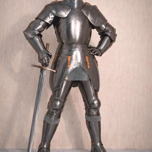 May include: A complete set of medieval armour, including a helmet, chest plate, and leg protection. The silver-coloured armour has detailed features. A long sword is held at the side. The text "Medieval Store" is in the upper right corner.