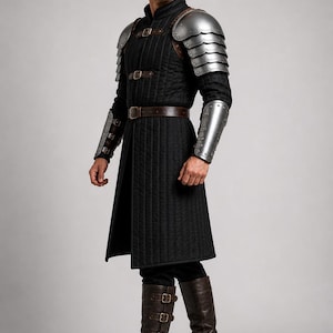 May include: A black quilted long-sleeved tunic with a high collar, worn with silver metal pauldrons and bracers, a brown leather belt, and dark brown leather boots with three buckles. The Medieval Store logo is visible in the top right corner.