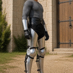 May include: A person wearing a grey long-sleeve shirt, black trousers, and a wide black leather belt. The outfit includes polished steel leg armor covering the thighs, knees, and shins, paired with matching steel gauntlets and pointed metal shoes.