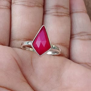 Op de afbeelding: Een zilveren ring met een opvallende, facetgeslepen, vlieger-vormige, robijnrode edelsteen. De ring is gezet op een zilveren band en wordt op een hand getoond.