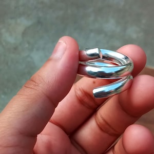 May include: A silver-colored ring with a spiral design. The ring appears to be made of a shiny metal and has a smooth, polished surface. The ring wraps around the finger in a continuous, flowing shape, creating a modern and minimalist aesthetic.