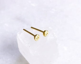 May include: A pair of gold stud earrings with a small, round, clear stone in the centre of each earring.
