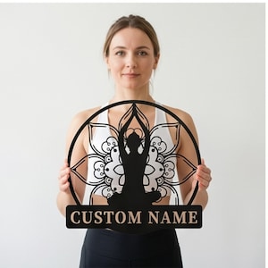 May include: A black circular wall sign featuring a silhouette of a person in a seated yoga pose centered within a detailed mandala pattern. Below the circular design is a rectangular plaque with the text CUSTOM NAME in capital letters.