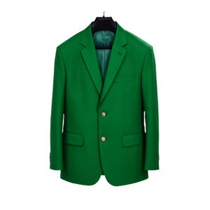 Op de afbeelding: Een felgroene blazer met goudkleurige knopen, hangend aan een zwarte hanger. De blazer heeft een klassieke sluiting met twee knopen, revers en voorzakken. De binnenvoering is een donkerdere tint groen.