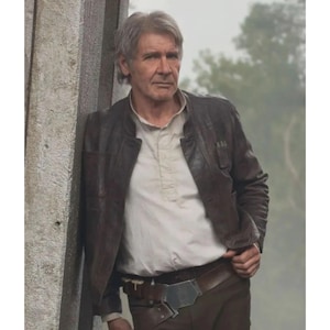 May include: A man in a brown leather jacket and a white shirt, leaning against a stone wall. The jacket has a worn look, and he's wearing brown trousers and a belt with a holster.