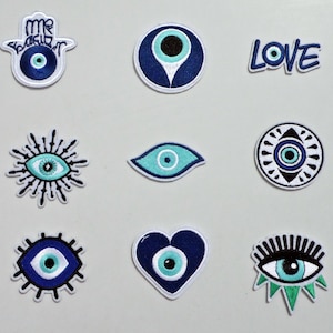 Könnte beinhalten: Neun gestickte Aufnäher mit dem Thema böses Auge. Die Aufnäher zeigen verschiedene Designs, darunter eine Hamsa-Hand, ein Herz und das Wort "LOVE". Die Farben sind Blau, Türkis, Schwarz und Weiß. Die Aufnäher sind wahrscheinlich für Kleidung oder Accessoires bestimmt.