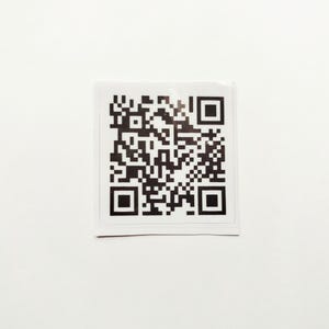 May include: A square sticker featuring a black and white QR code pattern. The design consists of a complex arrangement of small black squares and rectangles on a white background, including three distinct square alignment markers in the corners.