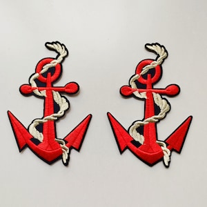 May include: Two embroidered patches featuring a red anchor design with a black outline. A white rope is wrapped around the anchor. The patches are on a white background. Nautical themed.