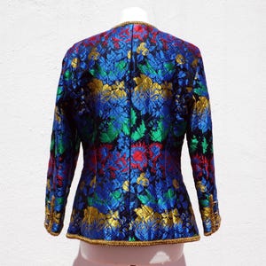 Pode incluir: Casaco vintage com um vibrante padr&atilde;o floral em azul, verde, vermelho e dourado. O casaco tem mangas compridas e uma borda dourada ao longo das bordas. A parte de tr&aacute;s do casaco &eacute; vis&iacute;vel, mostrando o design intrincado e a textura do tecido.