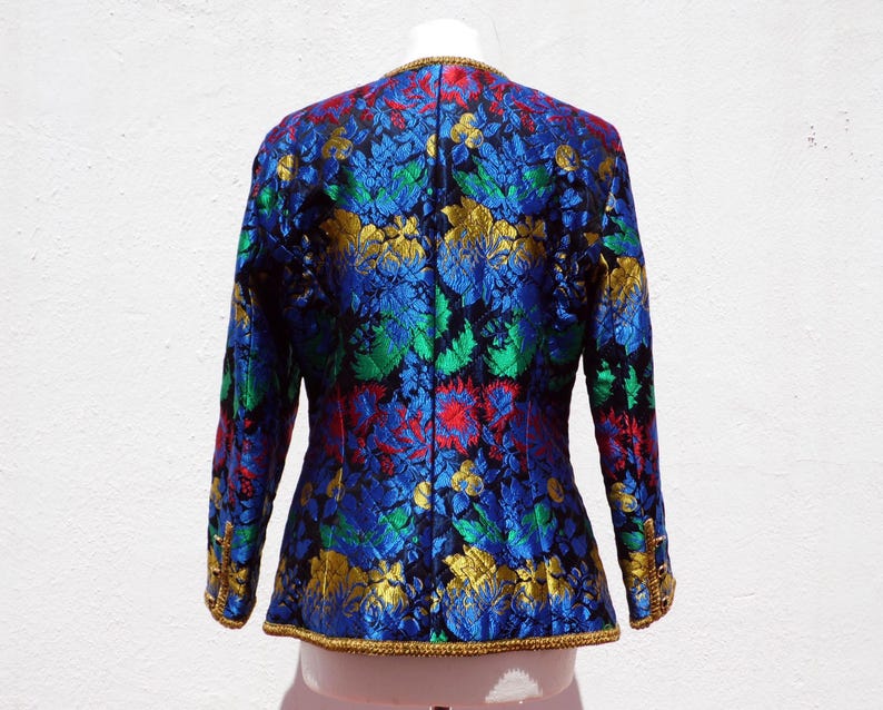 Pode incluir: Casaco vintage com um vibrante padr&atilde;o floral em azul, verde, vermelho e dourado. O casaco tem mangas compridas e uma borda dourada ao longo das bordas. A parte de tr&aacute;s do casaco &eacute; vis&iacute;vel, mostrando o design intrincado e a textura do tecido.