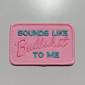 Può includere: Toppa rettangolare rosa ricamata con la frase "SOUNDS LIKE Bullshit TO ME" in filo turchese e rosa. La toppa ha un bordo rosa ed è destinata a vestiti o accessori.