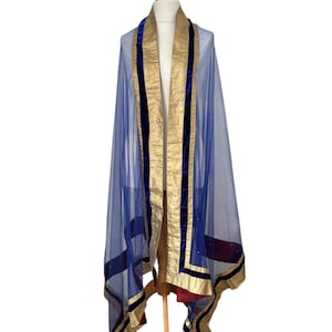 Puede incluir: Un dupatta azul transparente con ribetes dorados y azul marino, drapeado sobre un maniquí. El dupatta presenta ribetes dorados en los bordes y un borde azul marino. La tela es ligera y parece tener pequeños adornos brillantes.