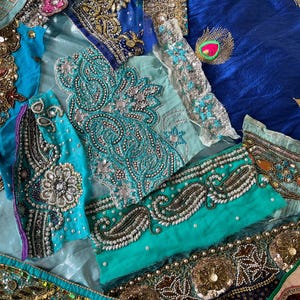Könnte beinhalten: Eine Sammlung verschiedener Stoffreste mit leuchtend blauen, türkisfarbenen und blaugrünen Textilien, die mit aufwendigen Metallstickereien, silbernen Pailletten, klaren Kristallen und bunten Perlen in Blumen- und Paisleymustern verziert sind.