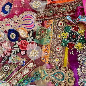 May include: A collection of assorted fabric patches and embroidered trims featuring vibrant colors like magenta, purple, gold, and teal. The pieces include floral motifs, paisley patterns, sequin embellishments, beadwork, and metallic thread accents.